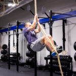 Man climbs rope in a fitness gym.