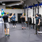 Members of gym, standing in a circle holding gym equipment.