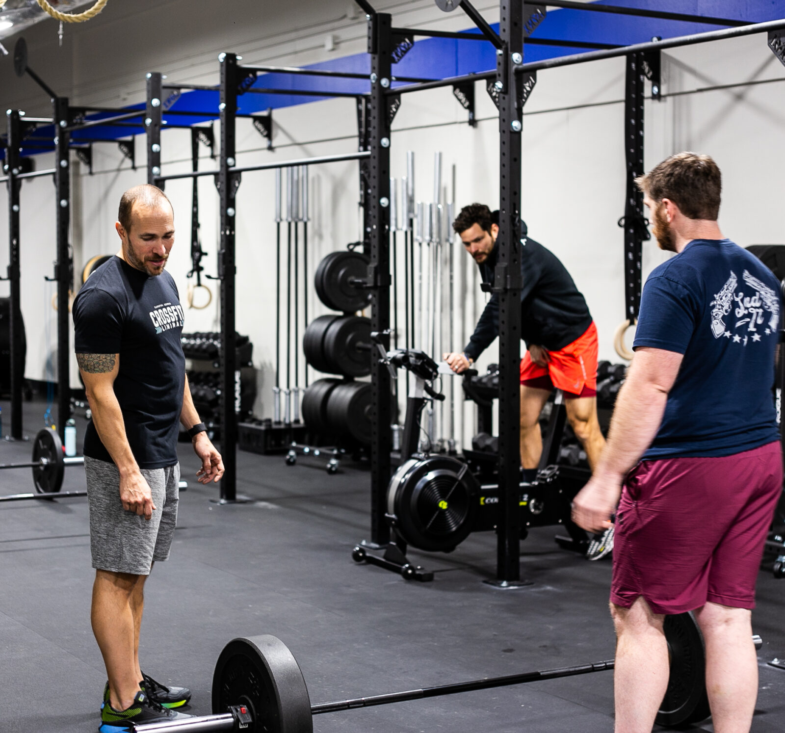 Trainer and two students lifting weights in a fitness gym.